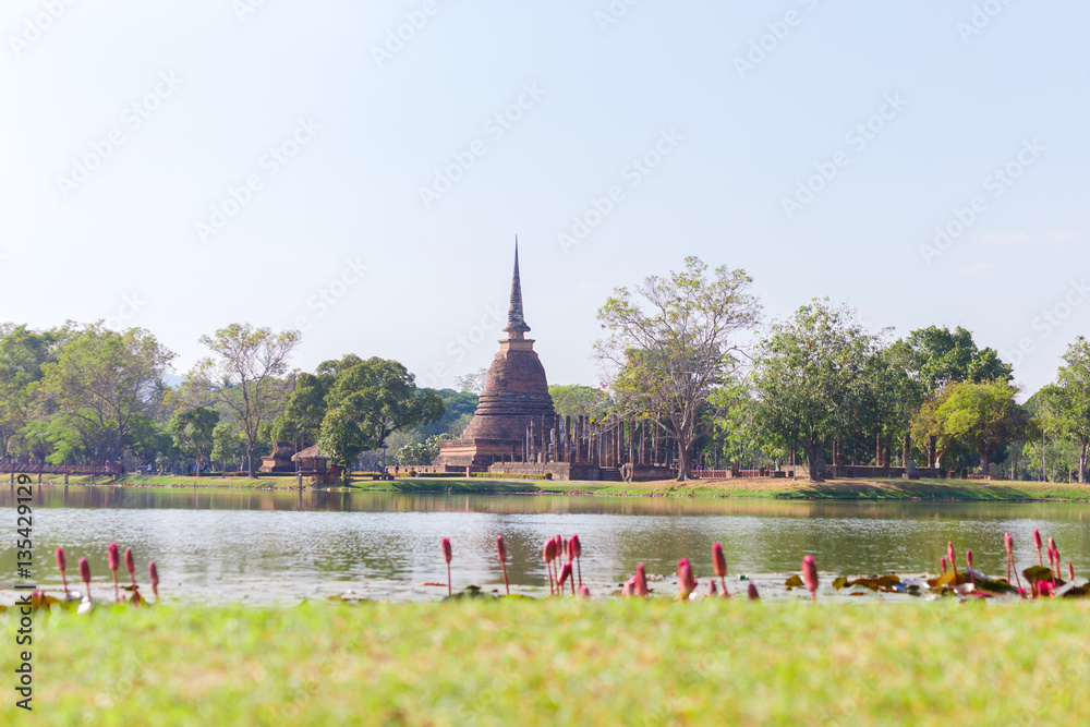 Obraz premium Ancient buddha statue and pagoda with lotus in the pool at Sukhothai Historical Park, Sukhothai Province, Thailand.