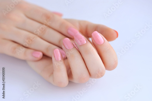 Closeup of hands of a young woman with pink manicure on nails against white background