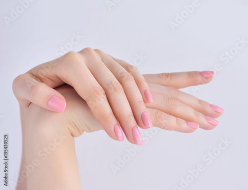Closeup of hands of a young woman with pink manicure on nails against white background