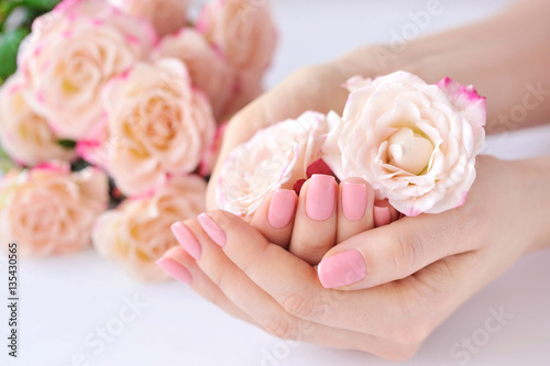 Hands of a woman with pink manicure on nails and roses