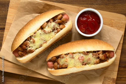 Baked chili hot dogs with ketchup on wooden board, photographed overhead with natural light