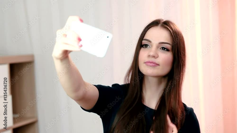 Portrait of a Beautiful successful smiling girl doing selfie in a black shirt on a light background Portrait of a Beautiful successful smiling girl doing selfie in a black shirt on a light background