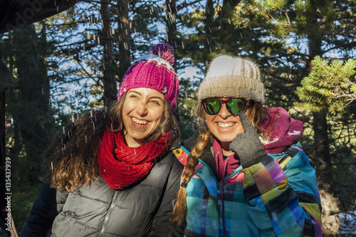 Two smiling women wearing warm clothes in a sunny snow fall wint