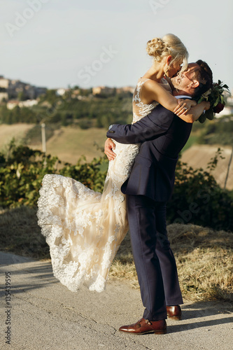 Groom raises up elegant bride while they stand on the road