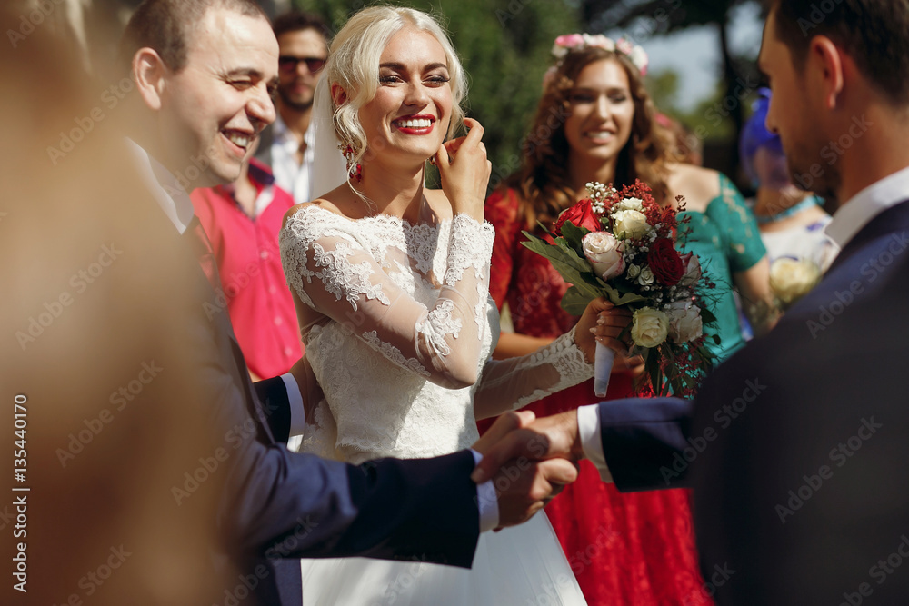 Father of a bride shakes man's hand while she stands between the