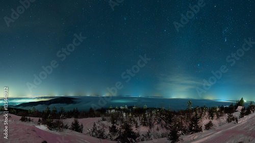 winter night sky above mountains with stars and city lights in the distance