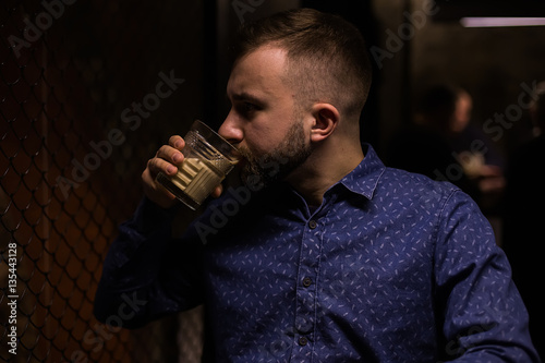 Business man, in blue shirt and glasses, drinking cocktail of vintage old fashion glass in loft bar