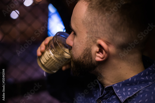 Business man, in blue shirt and glasses, drinking cocktail of vintage old fashion glass in loft bar