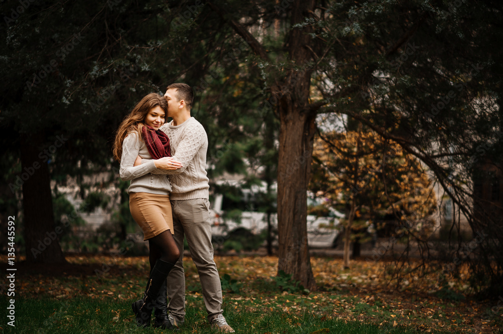 Young couple wearing on tied warm sweaters hugging in love at ci Young couple wearing on tied warm sweaters hugging in love at ci
