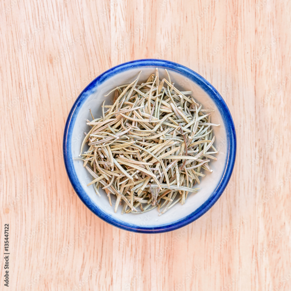 Dried rosemary in bowl on wood floor background. Dried rosemary in bowl on wood floor background.