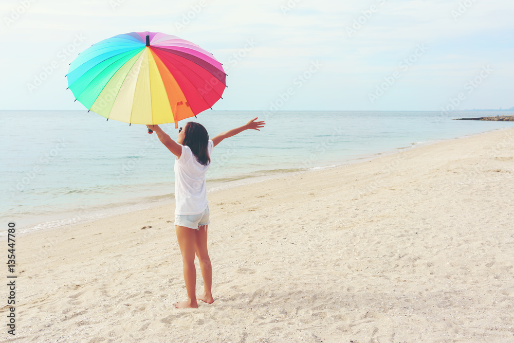 Asian young woman holding rainbow umbrella , feeling happy and  taking a deep breath on the beach 