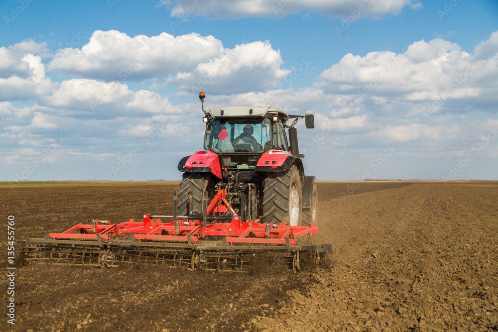 Obraz premium Farmer in tractor preparing land with seedbed cultivator