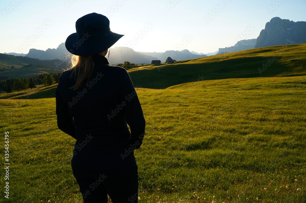 Wanderin genießt Morgensonne und Aussicht auf Wiese und Berge in Südtirol / Seiser Alm / Gröden Wanderin genießt Morgensonne und Aussicht auf Wiese und Berge in Südtirol / Seiser Alm / Gröden