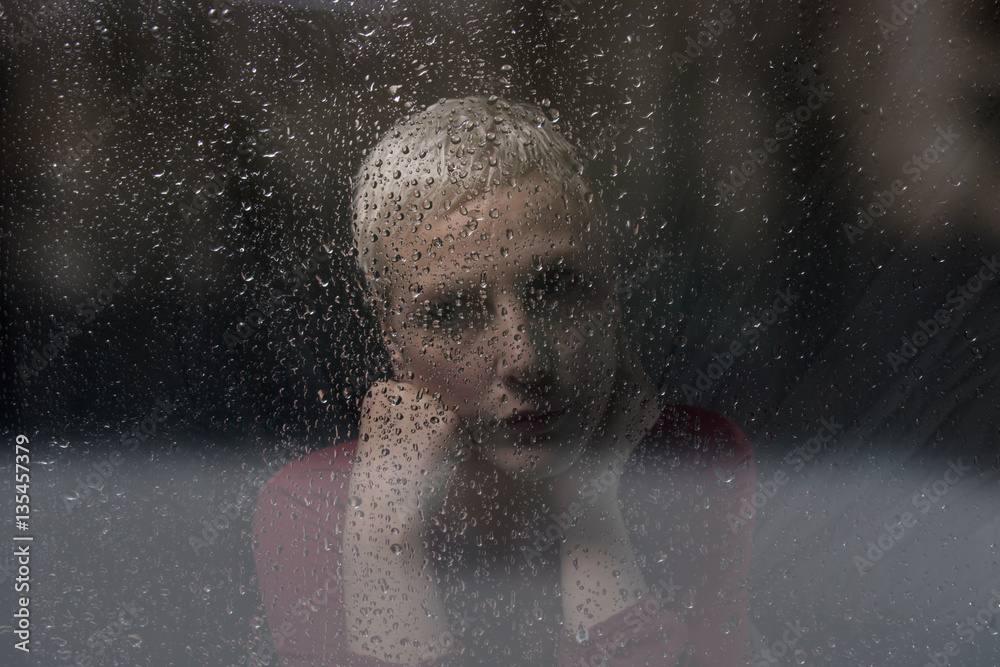 sad woman looks through window with raindrops
