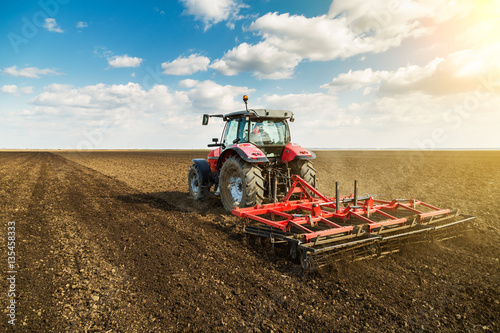 Farmer in tractor preparing land with seedbed cultivator as part of pre seeding activities in early spring season of agricultural works at farmlands. photo