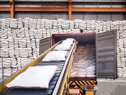 White bags of sugars from warehouse are staffing in container for export.