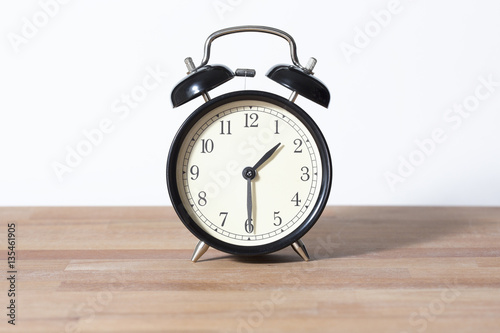 It is half past one o'clock. The time is 1:30. Retro clock isolated on a wooden table. White background.
