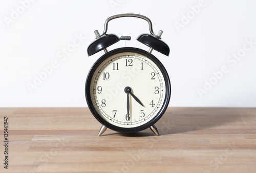 It is half past four o'clock. The time is 4:30. Retro clock isolated on a wooden table. White background.