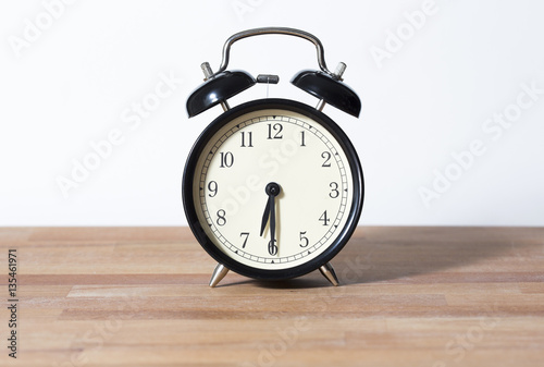 It is half past six o'clock. The time is 6:30. Retro clock isolated on a wooden table. White background.