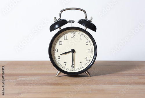 It is half past eight o'clock. The time is 8:30. Retro clock isolated on a wooden table. White background.
