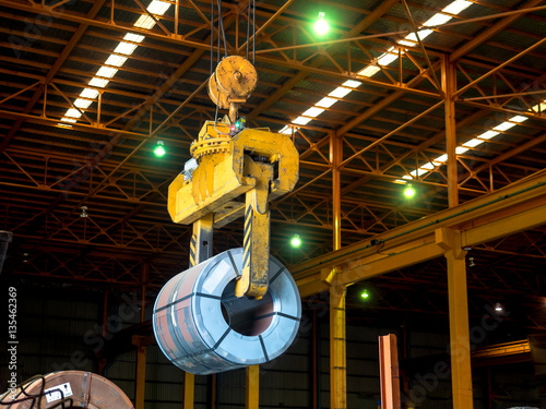 An overhead crane -Coil tong carrying a steel coil to a designated place in an automated warehouse storage facility.