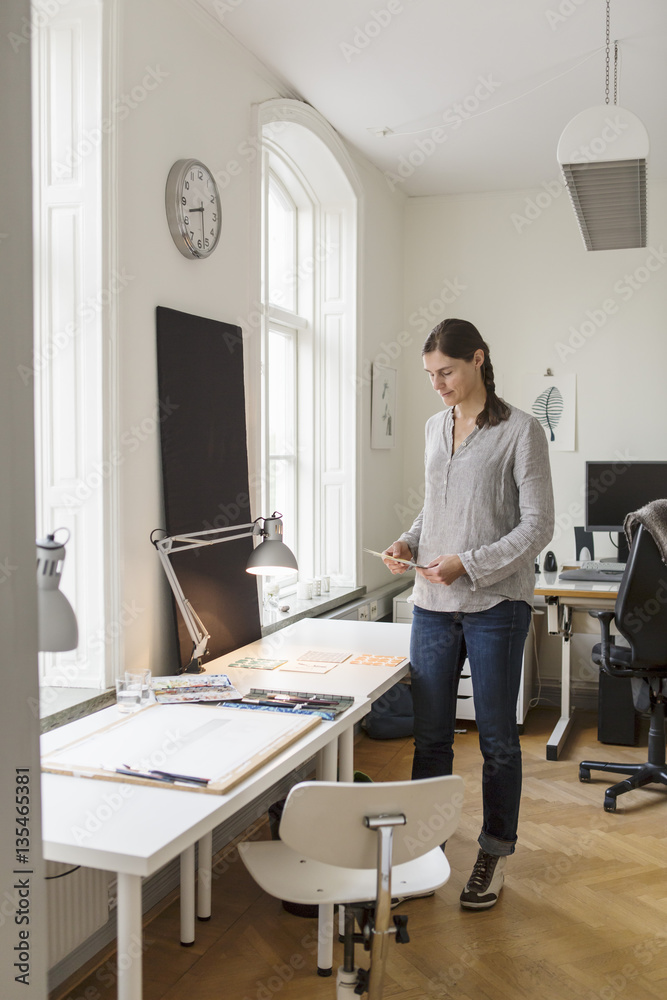 Full length of artist standing by table in creative office