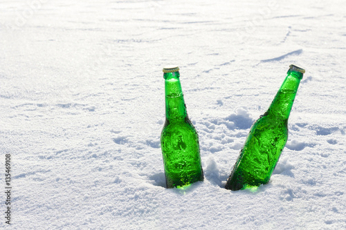 Two bottles of cold beer on the snow at sunset. Close up view.