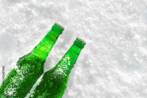 Two bottles of cold beer on the snow at sunset. Close up view.