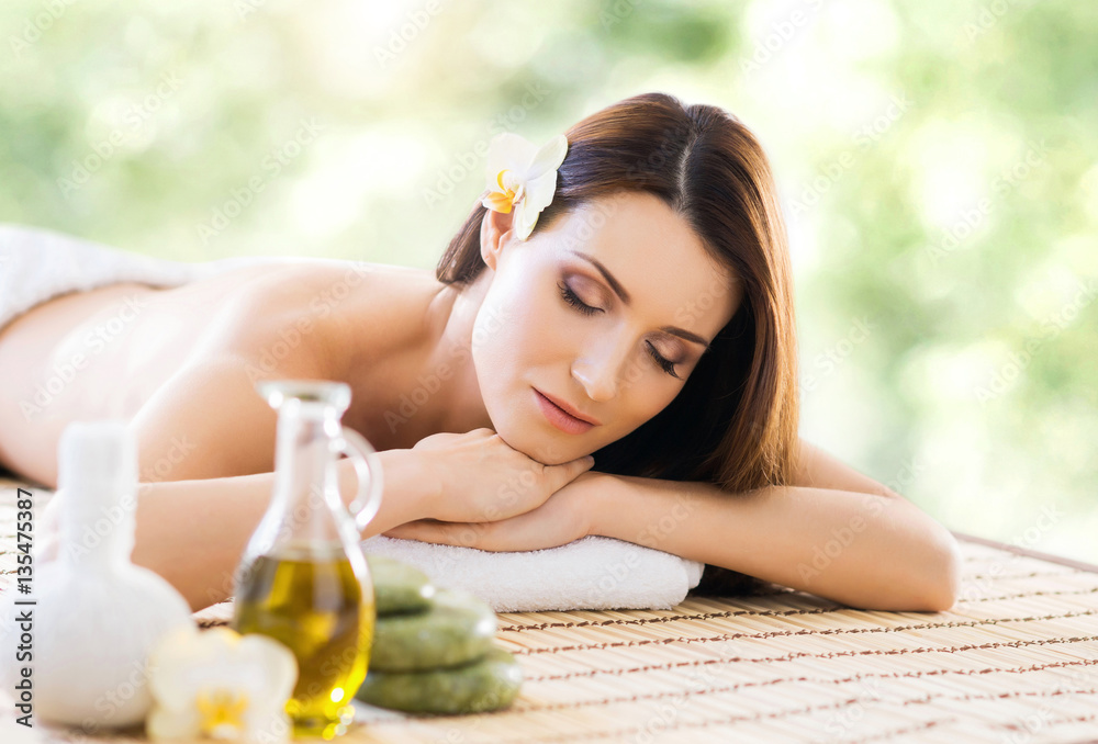 Naklejka premium Beautiful, young and healthy woman in spa salon. Massage treatment over green summer or spring background. Traditional medicine and healing concept.
