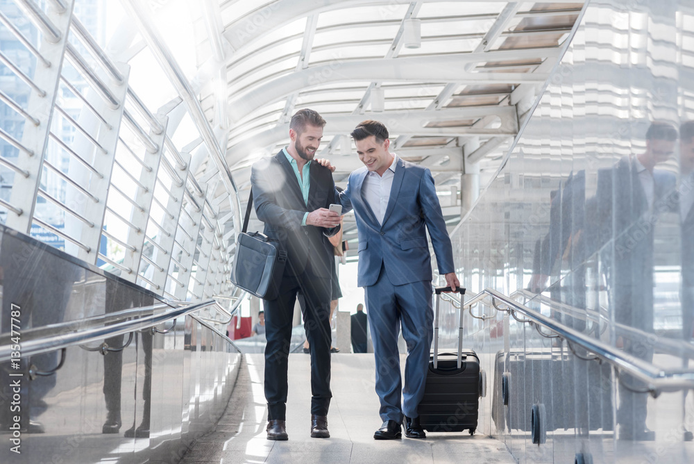 Two Westerner Business men talk and use smart phone on the publi Two Westerner Business men talk and use smart phone on the publi