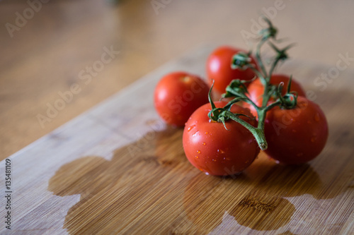 Fresh washed red cherry tomatoes on a wooden board. Close-up view. Red tomatos covered with water drops.