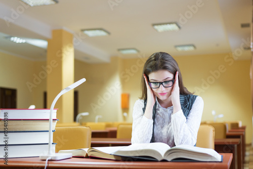 Young woman sitting by desk with stack of books placed on it, ho