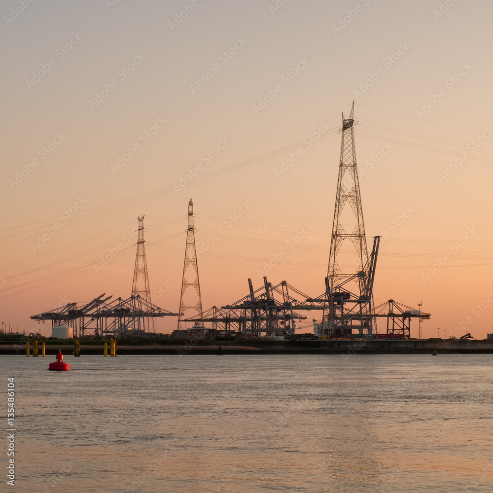 Electricity pylon against a sunset sky in front of a port terminal