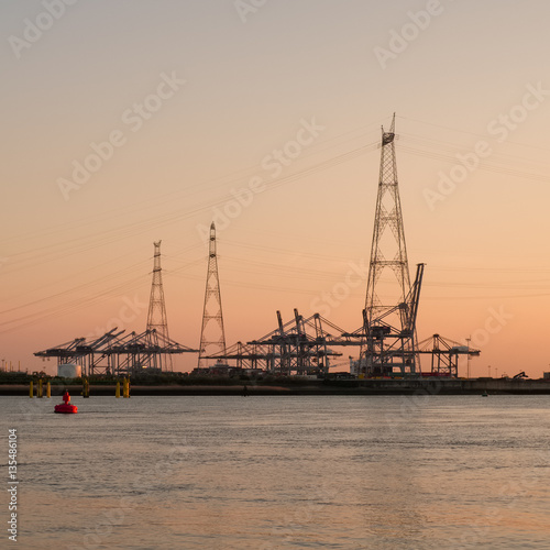 Electricity pylon against a sunset sky in front of a port terminal © Erik_AJV