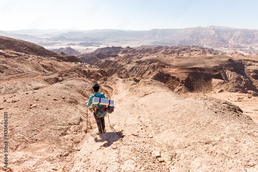 backpacker descending  hiking mountain ridge stone desert landscape.