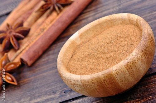 Cinnamon powder in a bowl with star anise and cinnamon sticks on table