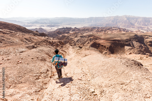 backpacker descending hiking mountain ridge stone desert landscape.