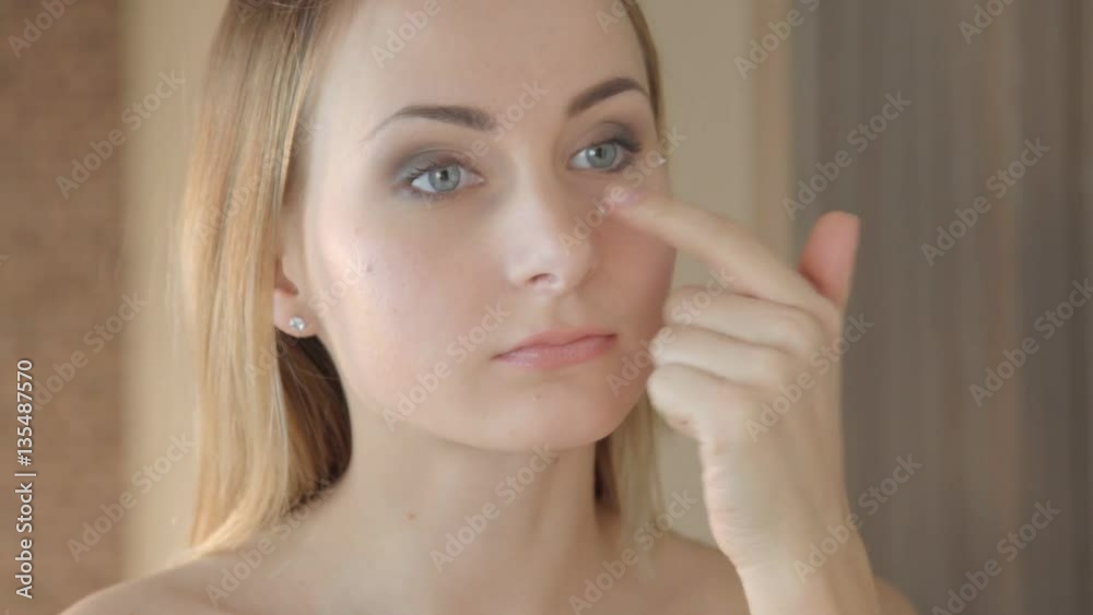 Beautiful young woman applying cream on face Beautiful young woman applying cream on face