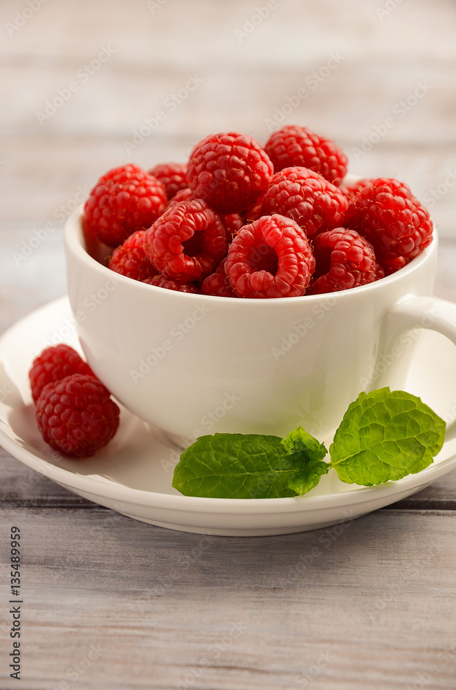 Ripe sweet raspberries in white cup on wooden table, selective focus, vertical, close up, copy space. Ripe sweet raspberries in white cup on wooden table, selective focus, vertical, close up, copy space.