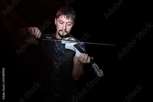 Young bearded violinist playing on electric violin white on a black background