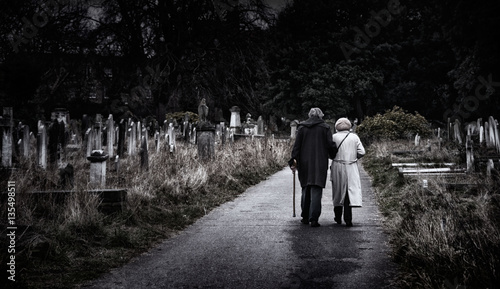 Brompton, London - An elderly couple walk hand-in-hand through a graveyard photo