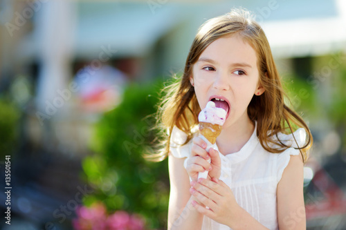 Adorable little girl eating tasty fresh ice cream outdoors