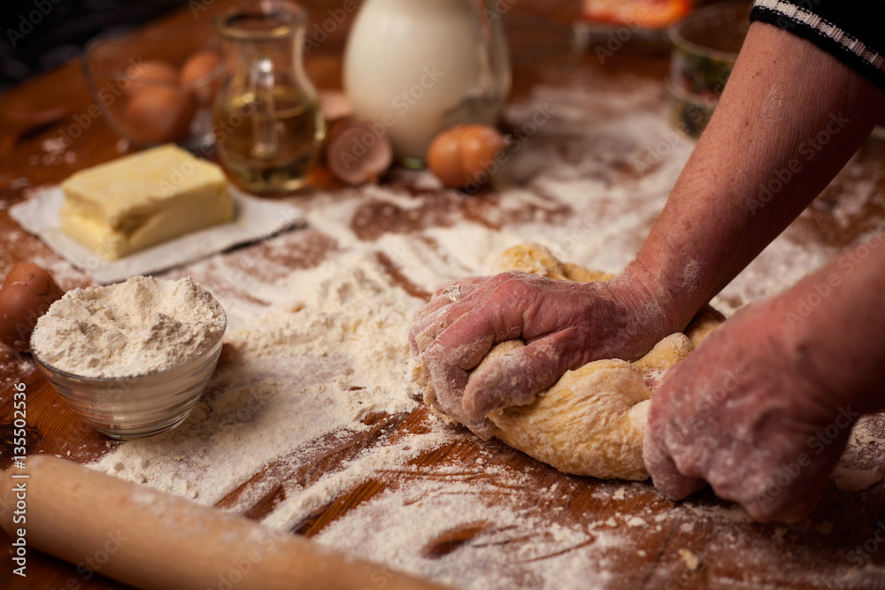Senior woman hands knead dough on  table in  home kitchen