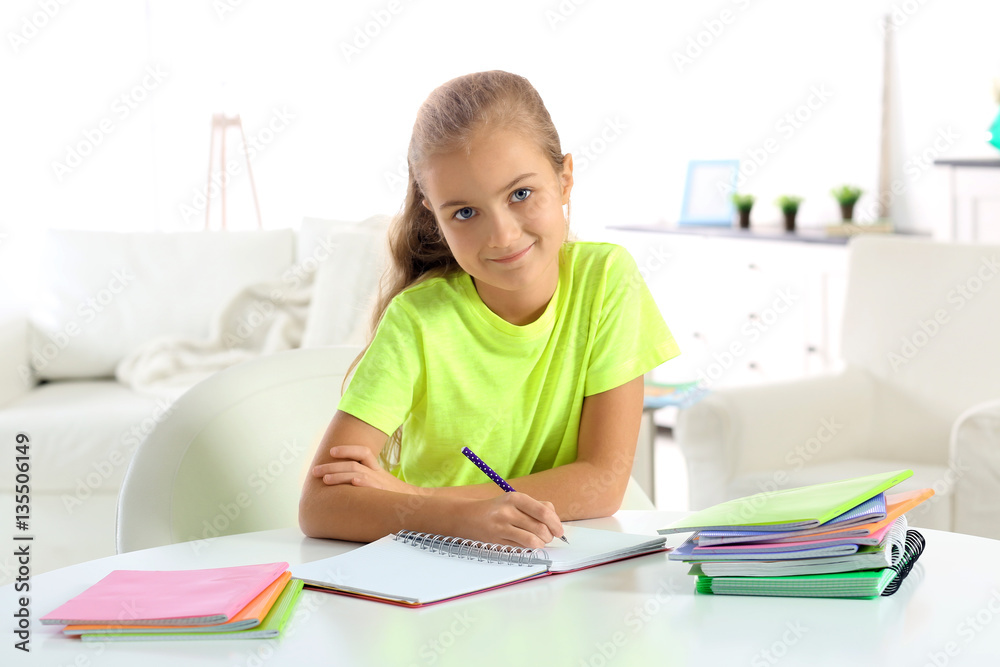 Attractive little girl sitting at table and doing home tasks Attractive little girl sitting at table and doing home tasks