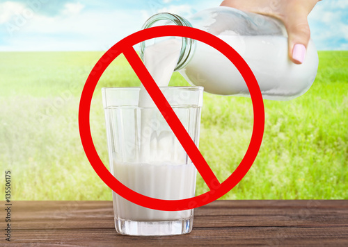 Allergic food products concept. Woman pouring milk from bottle into glass and restriction sign on nature background