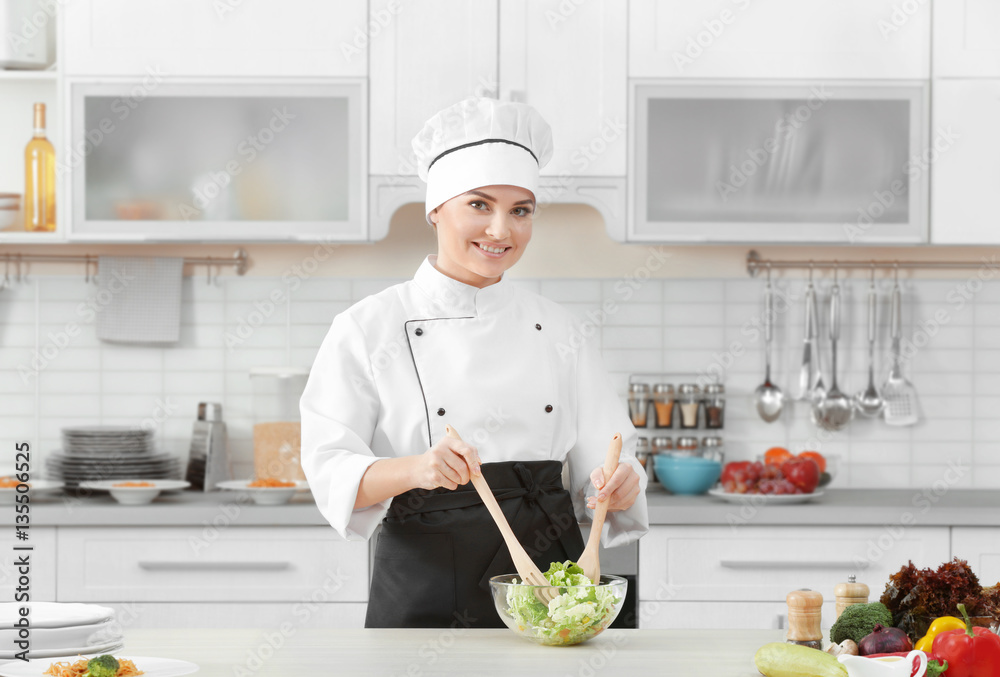 Young woman chef cooking salad in modern kitchen