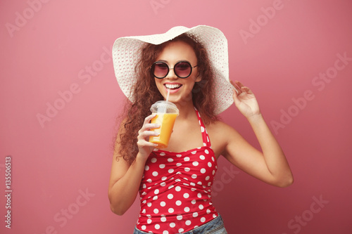 Young beautiful woman in hat with cocktail on color background