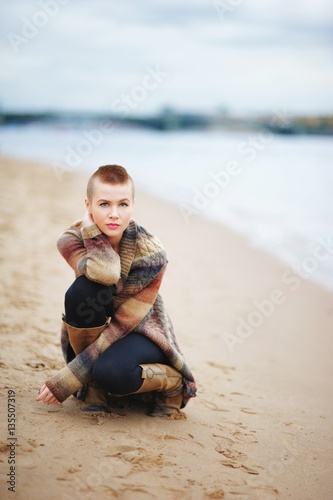 Beautiful, confident, girl with short hair squatted on the banks of the Neva. The concept of youth fashion