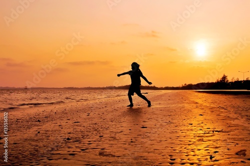 Silhouette of girl running on the beach at sunset