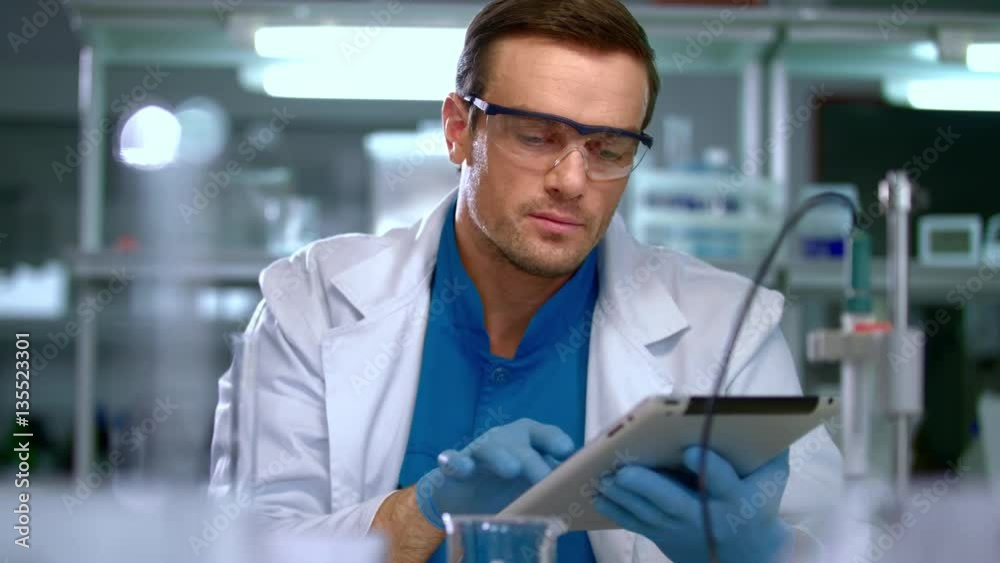 Young scientist using tablet pc in laboratory. Scientist searching data in modern laboratory. Young scientist working on computer equipment. Scientist man writing data on tablet pc in lab